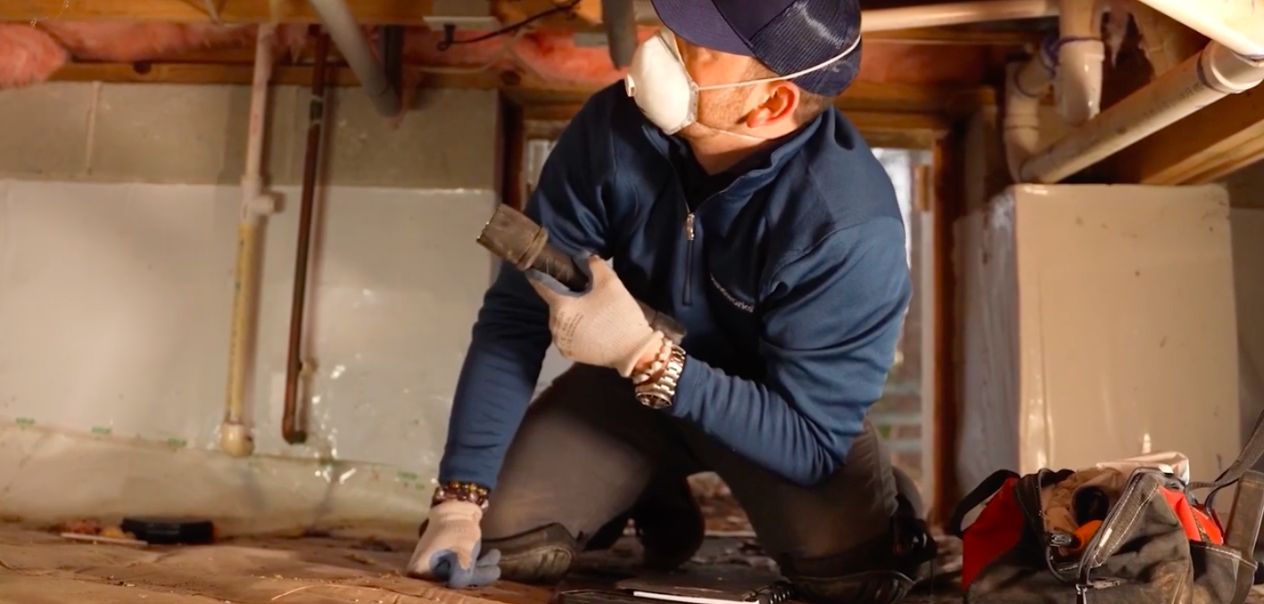Adjustable steel support jacks holding up wooden floor joists in a crawl space